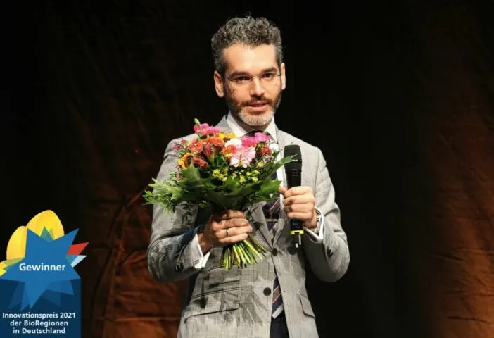 Young man with glasses, gray suit and holding with one hand a flower and with the other hand holding a microphone