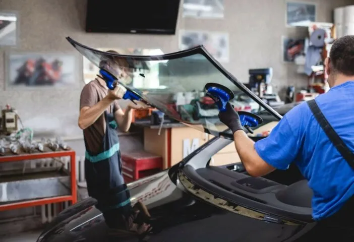 Two male mechanics holding a windsheald using tools