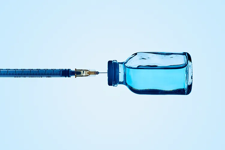 A syringe and a blue liquid in a vaccine bottle