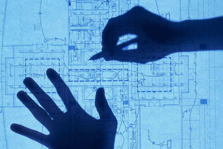 A photograph of a couple of hands drawing construction plans