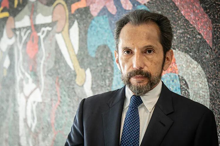 A photograph of Carlos Aguilar in front of a mural