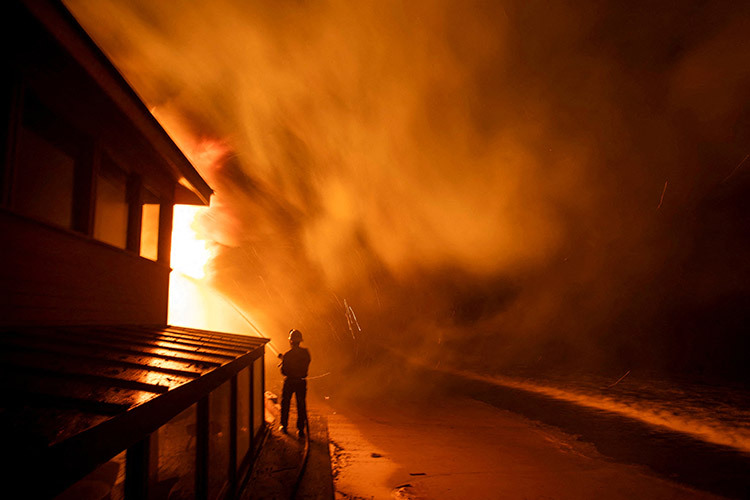 A firefighter works to contain the Palisades fire as it burns during a windstorm on Los Angeles' west side,