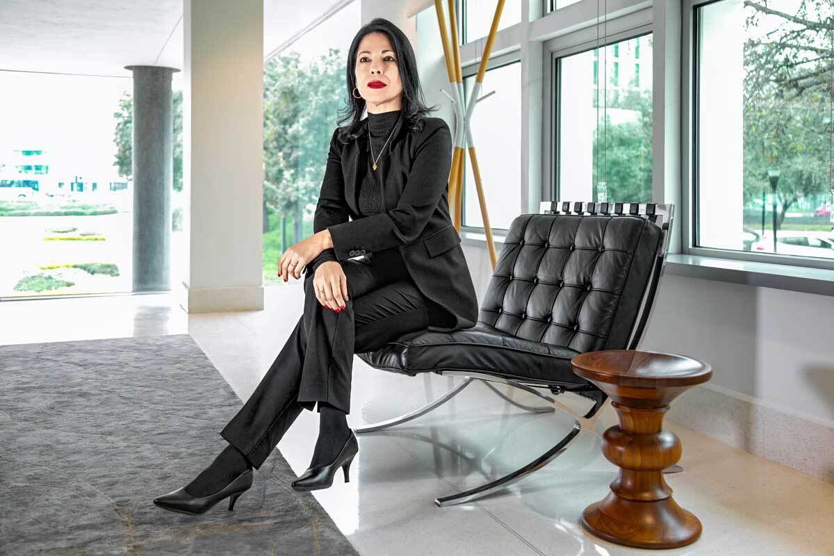 Empowered woman dressed in a black suit sitting on a Mies van Der Rohe chair.