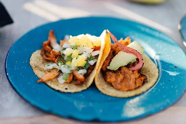 Photograph of Mexican al pastor tacos with pineapple on a blue plate