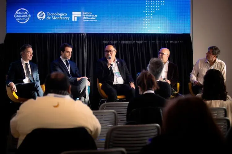 Photograph of five men sitting in chairs with a screen behind them