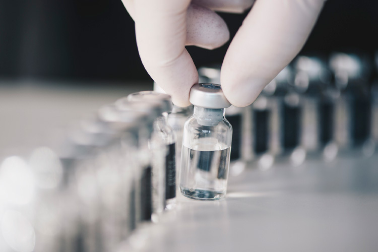 Photograph of glass vials, one of them held by a hand with a white glove
