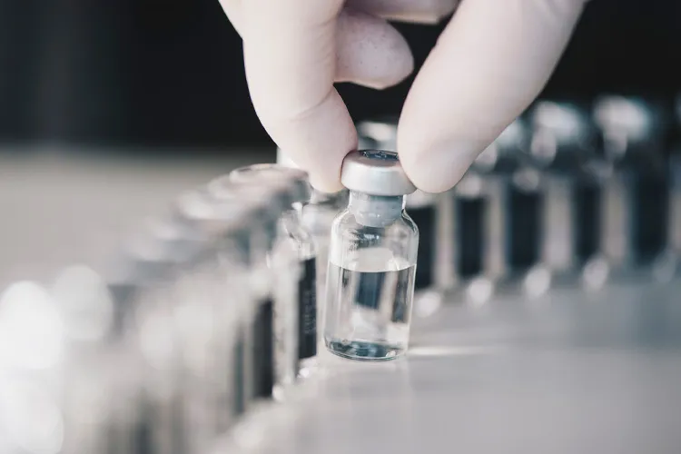 Photograph of glass vials, one of them held by a hand with a white glove