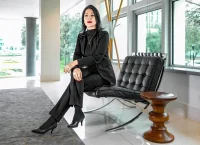 Empowered woman dressed in a black suit sitting on a Mies van Der Rohe chair.