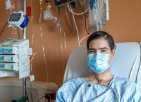 Photograph of a patient wearing a face mask in a hospital bed