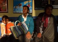 Photograph of two indigenous women and an indigenous girl sitting in a waiting room