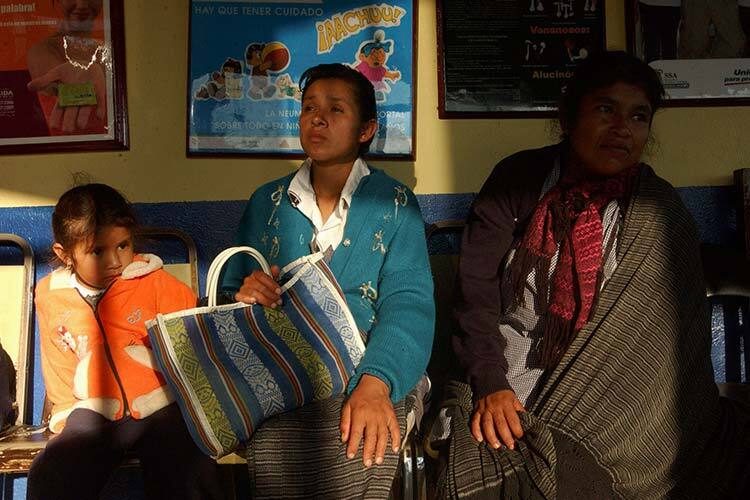 Photograph of two indigenous women and an indigenous girl sitting in a waiting room