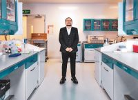 Man wearing a blue suit standing in the middle of a laboratory