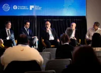 Photograph of five men sitting in chairs with a screen behind them