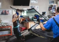 Two male mechanics holding a windsheald using tools