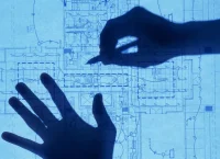 A photograph of a couple of hands drawing construction plans