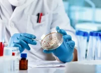 Image of a person wearing gloves and a lab coat in a laboratory, holding a lab container.