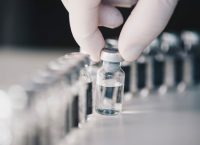 Photograph of glass vials, one of them held by a hand with a white glove
