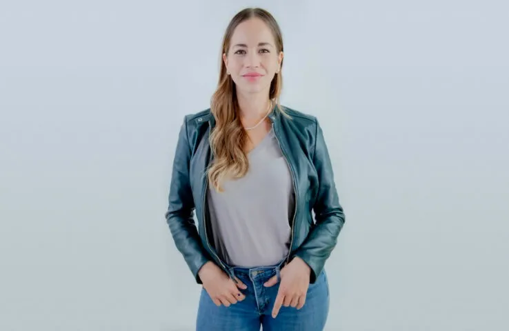 Mujer cabello rubio vistiendo chamarra negra y camiseta gris