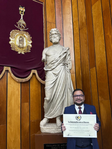 Hombre sosteniendo un diploma, frente a una estatua de Hipócrates