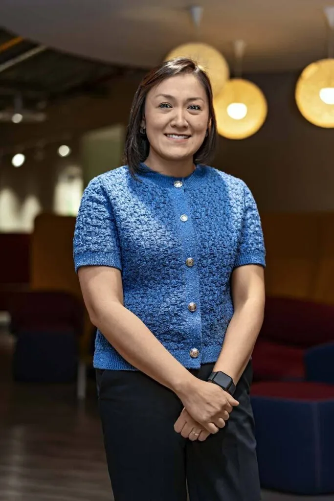 Mujer sonriendo con blusa azul y agarrandose las manos. 