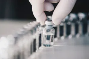 Fotografía de viales de vidrio, uno de ellos sostenido por una mano con un guante blanco