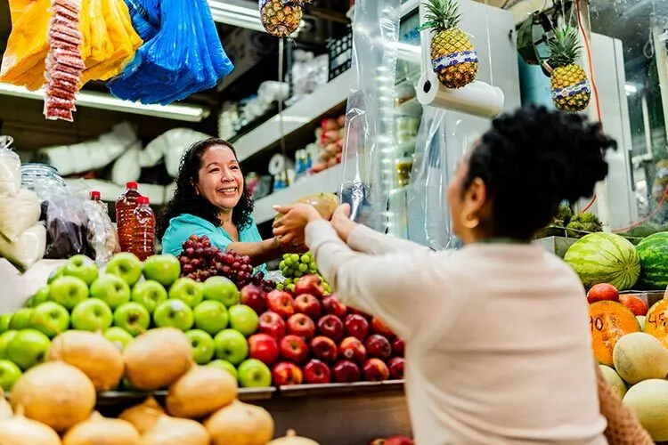 un puesto de fruta donde se ve a una mujer comprando