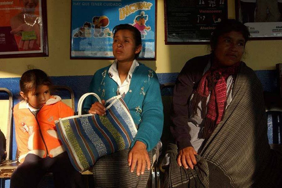 Fotografía de dos mujeres indígenas y una niña indígena sentadas en una sala de espera