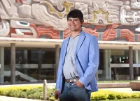 Hombre con saco azul posa en frente de un mural