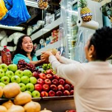 un puesto de fruta donde se ve a una mujer comprando