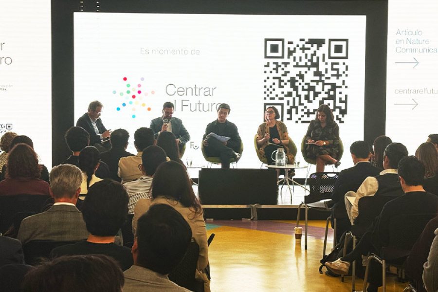 Panel de cinco personas sentadas en un escenario frente a una audiencia, con una pantalla de fondo que muestra el logo "Centrar el Futuro" y un código QR.