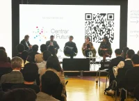Panel de cinco personas sentadas en un escenario frente a una audiencia, con una pantalla de fondo que muestra el logo "Centrar el Futuro" y un código QR.