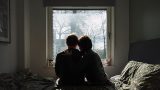 imagen de una pareja sentada en una cama, viendo a una ventana