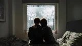 imagen de una pareja sentada en una cama, viendo a una ventana