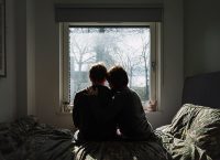 imagen de una pareja sentada en una cama, viendo a una ventana