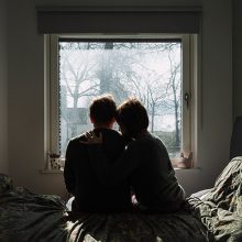 imagen de una pareja sentada en una cama, viendo a una ventana