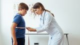 imagen de una doctora mujer con una bata, en un consultorio, midiendo la cintura de un niño con una cinta métrica