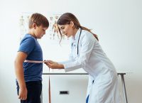 imagen de una doctora mujer con una bata, en un consultorio, midiendo la cintura de un niño con una cinta métrica
