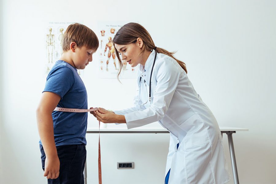 imagen de una doctora mujer con una bata, en un consultorio, midiendo la cintura de un niño con una cinta métrica