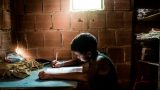 imagen de un cuarto oscuro, de ladrillos, donde se ve a una niña escribiendo en un cuaderno