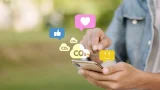 se ve a un usuario de celular tocando una pantalla de donde se ve que salen íconos de corazones y nubes que dicen CO2