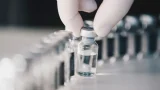 Fotografía de viales de vidrio, uno de ellos sostenido por una mano con un guante blanco