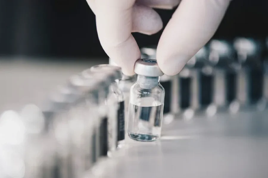 Fotografía de viales de vidrio, uno de ellos sostenido por una mano con un guante blanco
